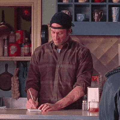 A Man Is Writing On A Notepad In Front Of A Shelf With Ketchup GIF