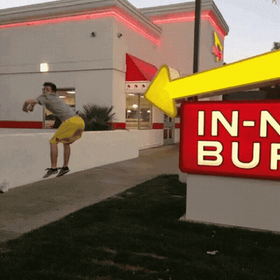 A Man Jumps In The Air In Front Of An In-N-Out Burger Sign GIF