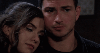 A Man Kisses A Woman On The Cheek While They Sit On A Bed GIF
