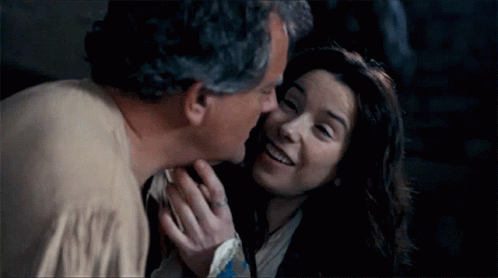 A Man Kissing A Woman On The Cheek In A Dark Room . GIF