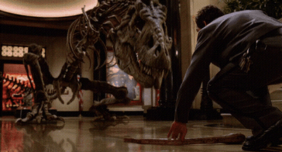 A Man Kneeling Down In Front Of A Dinosaur Skeleton With The Number 8888 On The Wall Behind Him GIF