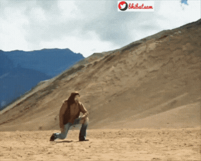 A Man Kneeling Down In The Desert With A Sign That Says Bhibat.com Behind Him GIF