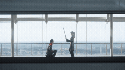 A Man Kneeling Down With A Woman Holding A Stick In Front Of A Large Window GIF