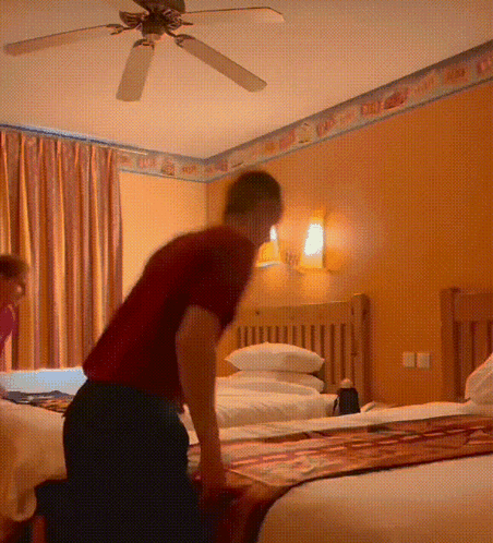 A Man Kneeling On A Bed In A Hotel Room GIF