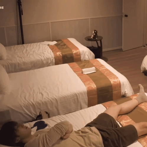 A Man Laying On A Bed In A Hotel Room With The Word Be On The Wall GIF