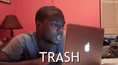 A Man Laying On A Bed Looking At A Laptop With The Word Trash Written On The Screen GIF