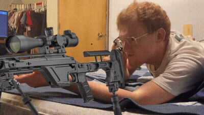 A Man Laying On A Bed Looking At A Rifle GIF