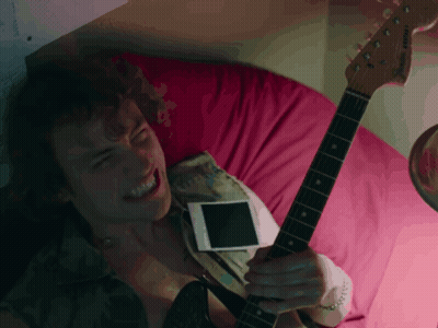 a man laying on a bed with a guitar and a cell phone