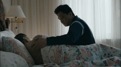 A Man Laying On A Bed With A Lamp Behind Him GIF