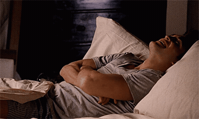 A Man Laying On A Bed With His Arms Crossed And His Mouth Open GIF
