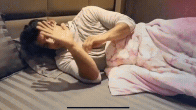 A Man Laying On A Bed With His Hand On His Face GIF
