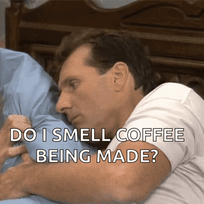 A Man Laying On A Bed With The Words " Do I Smell Coffee Being Made " Above Him GIF