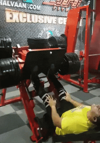 A Man Laying On A Bench In A Gym With A Sign That Says Exclusive GIF