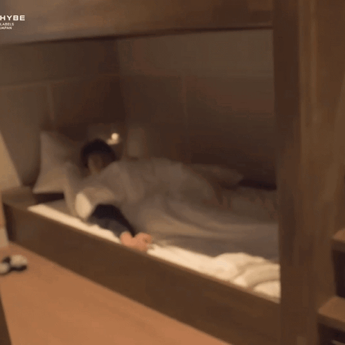 A Man Laying On A Bunk Bed With The Word Hybe On The Bottom Right GIF
