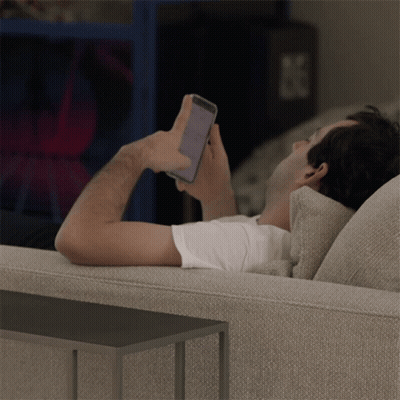 A Man Laying On A Couch Looking At A Cell Phone GIF