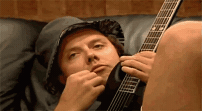 A Man Laying On A Couch Playing A Guitar . GIF