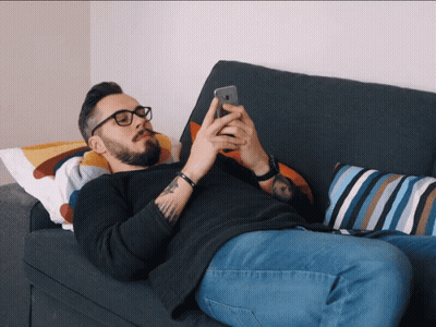 A Man Laying On A Couch Using A Cell Phone GIF