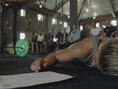 A Man Laying On The Floor With A Green Barbell That Says ' Rogue ' On It In Front Of A Crowd GIF