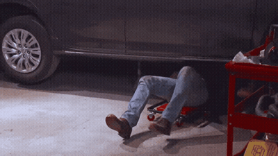 A Man Laying Under A Car In A Garage With A Sign That Says ' A ' On It GIF