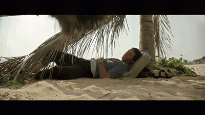 A Man Laying Under A Palm Tree On The Beach GIF