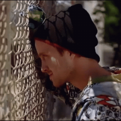 A Man Leaning Against A Chain Link Fence Wearing A Beanie And Sunglasses GIF