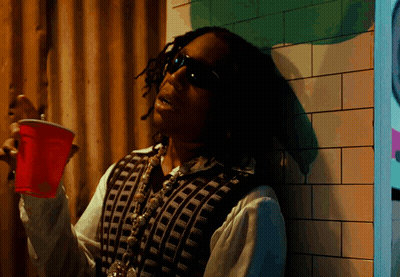 A Man Leaning Against A Wall Holding A Red Plastic Cup GIF