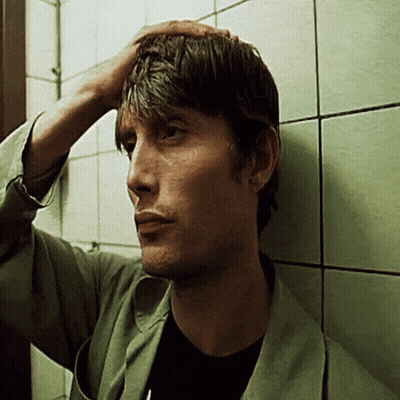 A Man Leaning Against A Wall Holds His Hand To His Head GIF