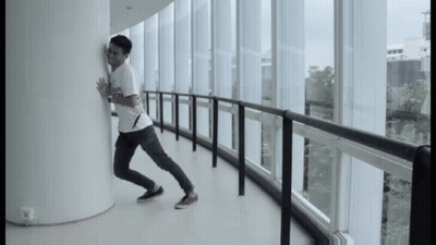 A Man Leaning Against A Wall In A Hallway With Lots Of Windows GIF