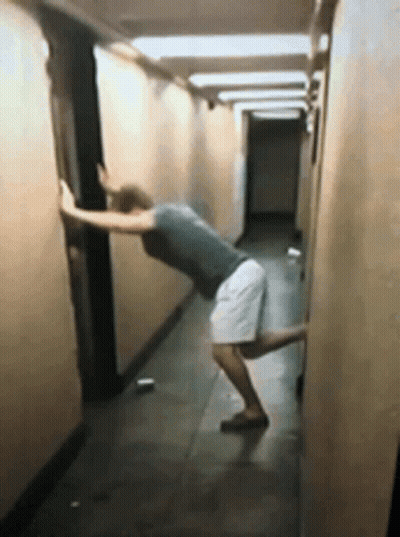 A Man Leaning Against A Wall In A Long Hallway GIF