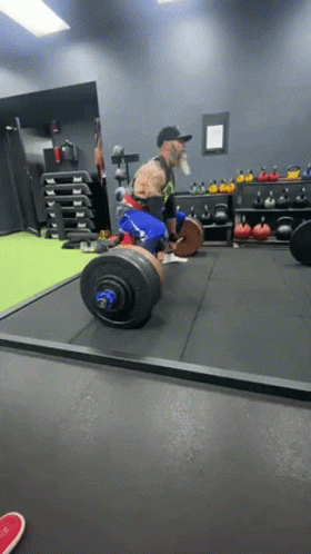 A Man Lifting A Barbell In A Gym With A Motorcycle In The Background GIF