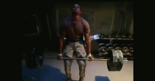 A Man Lifts A Barbell In A Dark Room GIF