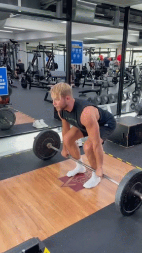 A Man Lifts A Barbell In A Gym While Wearing A Black Tank Top That Says ' Alpha ' On It GIF