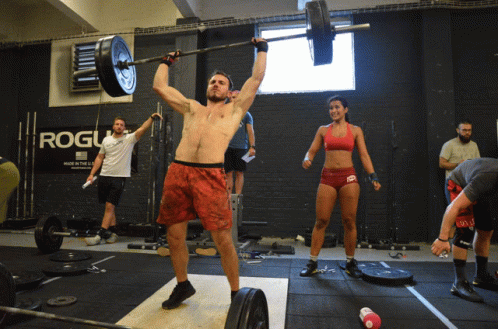 A Man Lifts A Barbell Over His Head In Front Of A Rogue Sign GIF