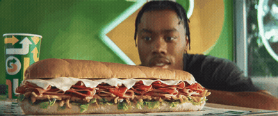 A Man Looking At A Subway Sandwich Next To A Cup That Says " Get " GIF