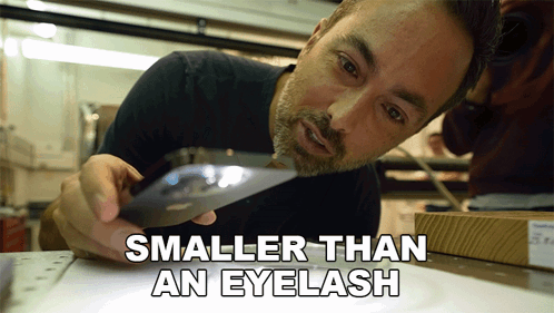 A Man Looking At Something Under A Magnifying Glass With The Words Smaller Than An Eyelash Below Him GIF
