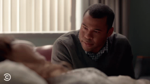 A Man Looks At A Woman Laying In A Hospital Bed With A C On The Bottom GIF