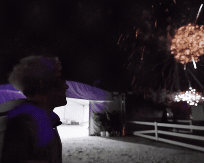 A Man Looks Up At A Fireworks Display In The Night Sky GIF