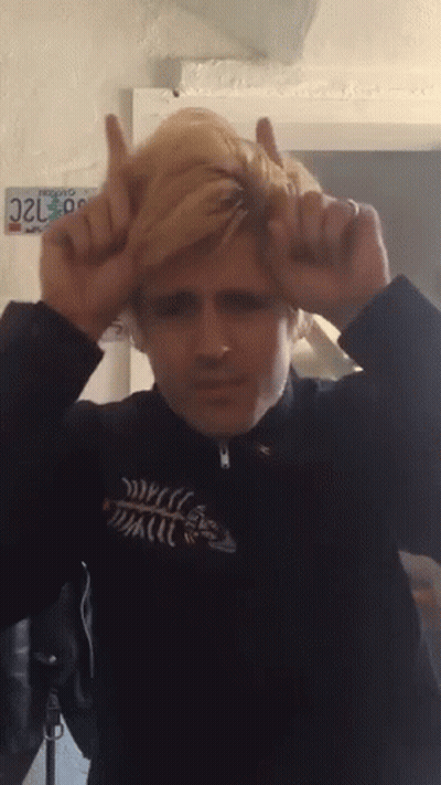 A Man Making A Devil Horns Gesture With A California License Plate Behind Him GIF