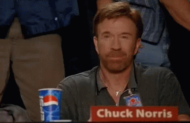 A Man Named Chuck Norris Is Sitting At A Table With His Fist In The Air GIF