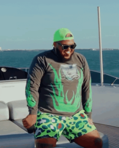 A Man On A Boat Wearing A Green Shirt And Leopard Print Shorts GIF
