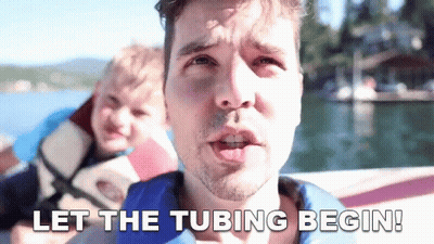 A Man On A Boat With The Words Let The Tubing Begin Below Him GIF