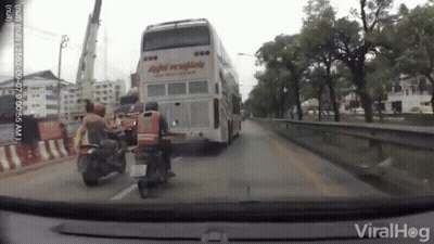 A Man On A Motorcycle Is Standing In Front Of A Double Decker Bus . GIF