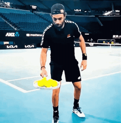 A Man On A Tennis Court Holding A Tennis Racquet And Balls GIF