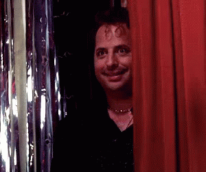A Man Peeking Out From Behind A Red Curtain And Smiling GIF