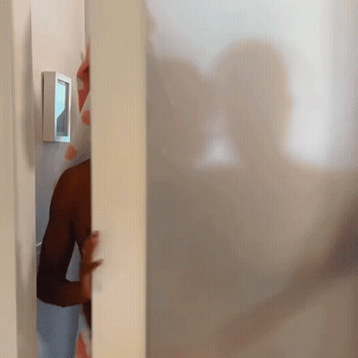 A Man Peeking Out From Behind A White Wall With A Picture Frame On It GIF