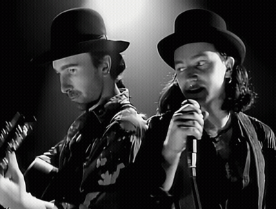 A Man Playing A Guitar And A Man Singing Into A Microphone In A Black And White Photo GIF