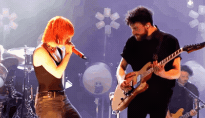 A Man Playing A Guitar And A Woman Singing Into A Microphone GIF