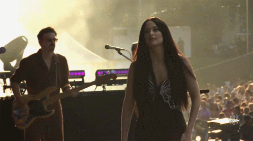 A Man Playing A Guitar And A Woman Singing On Stage GIF