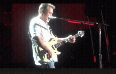 A Man Playing A Guitar And Singing Into A Microphone On A Stage GIF