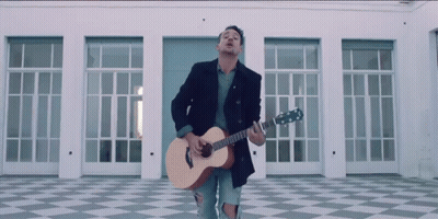 A Man Playing A Guitar In Front Of A Building GIF